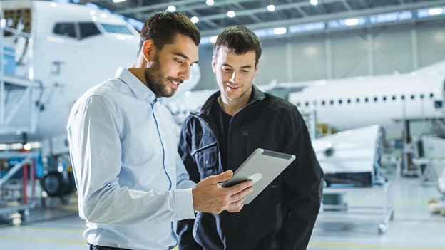 Two men in airplane hanger talking and looking at a tablet